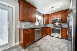 Kitchen featuring wood cabinetry, stainless steel appliances, dark countertops, and a subway tile backsplash - 