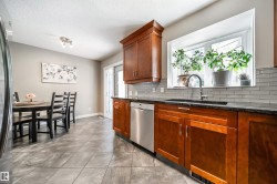 Kitchen featuring wood cabinetry, black countertops, stainless steel appliances, a subway tile backsplash, and a large window above the sink - 