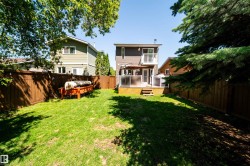 Expansive grassy yard featuring a wood deck, glass panel railing, and a private wood fence - 