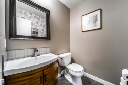 Powder room featuring a curved wood-finish vanity with an integrated white sink, brushed nickel faucet, and a white subway tile backsplash - 