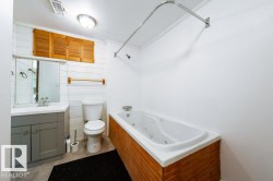 Bathroom featuring a white jetted tub, a gray vanity with an integrated sink, and white shiplap walls - 