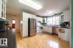 Kitchen featuring light wood-finish flooring, white cabinetry, dark countertops, a stainless steel French door refrigerator, and a stainless steel dishwasher - 
