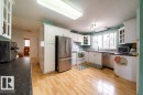 Kitchen featuring light wood-finish flooring, white cabinetry, dark countertops, a stainless steel French door refrigerator, and a stainless steel dishwasher - 4224 89 Street, Edmonton, AB 