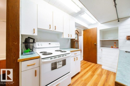 Kitchen featuring white cabinetry with wood-finish hardware, a white electric range, and wood-finish flooring - 4224 89 Street, Edmonton, AB 
