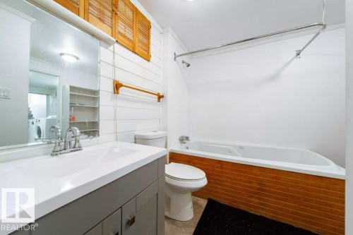 Bathroom featuring a vanity with a white countertop and chrome faucet, a toilet, a jetted tub with wood-finish paneling, and shiplap wall detailing - 4224 89 Street, Edmonton, AB 