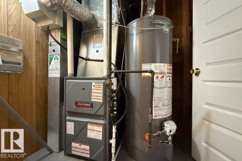 Utility area featuring a water heater and furnace with exposed ductwork and piping - 4224 89 Street, Edmonton, AB 