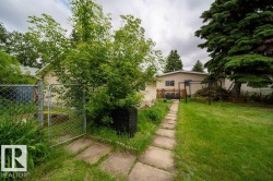 Expansive backyard featuring a stone pathway, mature trees, and a chain-link fence - 