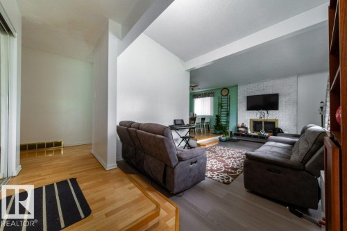 Open-concept living area featuring a whitewashed brick fireplace surround, a wood-finish flooring entry, and neutral wall tones - 4224 89 Street, Edmonton, AB 