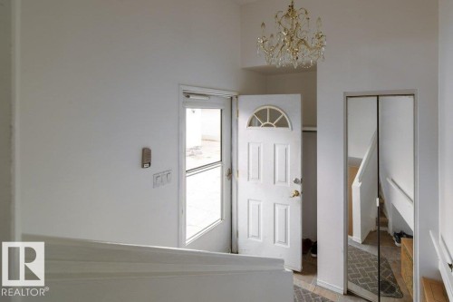 Foyer featuring a decorative chandelier and a solid wood front door with an arched transom window - 4224 89 Street, Edmonton, AB 