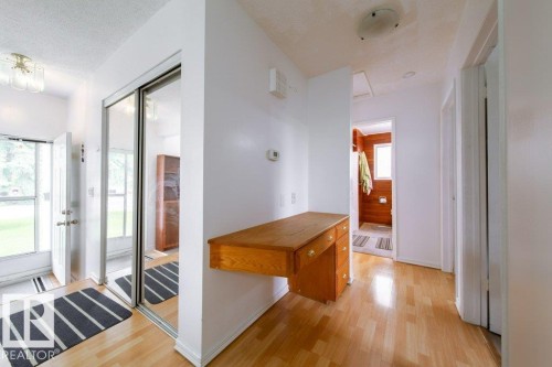 Entryway featuring wood-finish flooring, a built-in wooden desk with drawers, and a mirrored closet with sliding doors - 4224 89 Street, Edmonton, AB 