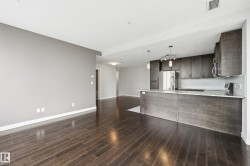 Open-concept living space featuring wood-finish flooring, a kitchen island with stone countertops, dark wood-finish cabinetry, stainless steel appliances, and a tiled backsplash - 