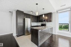 Modern kitchen featuring dark wood-finish cabinetry, stainless steel appliances, a center island with a light-toned countertop, and pendant lighting - 