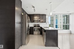 Kitchen featuring dark wood-finish cabinetry, stainless steel appliances, a center island with pendant lighting, and a window framing urban architecture - 