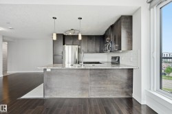 Open-concept kitchen featuring an island with a light-toned countertop, dark wood-finish cabinetry, stainless steel appliances, and a subway tile backsplash - 