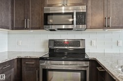 Kitchen featuring dark wood cabinetry, stainless steel appliances, light subway tile backsplash, and stone countertops - 