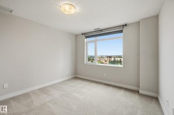 Carpeted room featuring a large window with roller shade, neutral wall paint, white trim, and a ceiling-mounted light fixture - 