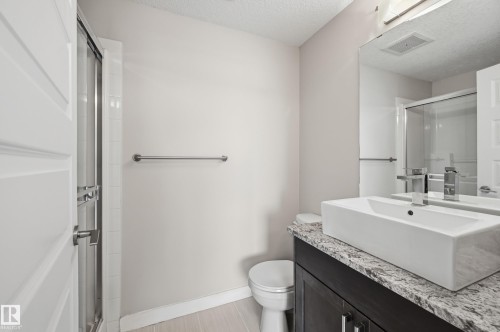 Bathroom featuring a dark wood-finish vanity with a stone countertop, a white rectangular vessel sink, and a chrome faucet - 528 5151 Windermere Boulevard, Edmonton, AB 