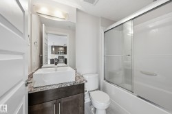 Contemporary bathroom featuring a vessel sink, dark wood-finish vanity, light-toned countertop, and a shower-tub combination with a sliding glass enclosure - 