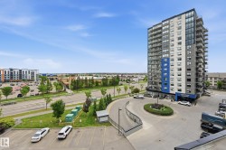 Modern high-rise building featuring a striking blue and gray exterior, multiple balconies, a circular driveway with landscaping, and an adjacent parking area - 