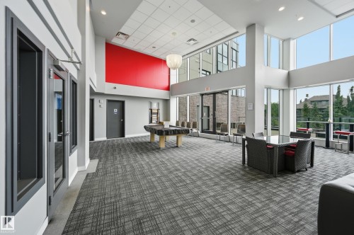 Spacious common area featuring extensive glazing, high ceilings, patterned carpet flooring, and a red accent wall - 528 5151 Windermere Boulevard, Edmonton, AB 