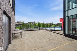 Spacious outdoor patio area featuring large format paver tiles, a glass and metal railing system, and a recreational court - 