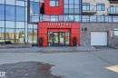 Building entrance featuring red paneling, clear glass double doors, a white overhead garage door, and stone facade accents - 528 5151 Windermere Boulevard, Edmonton, AB 