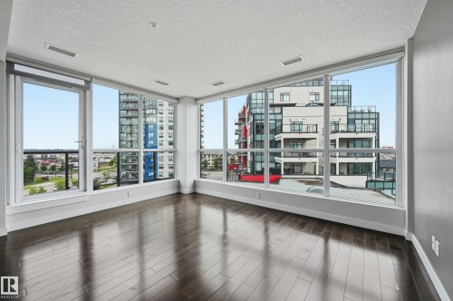 Spacious room featuring extensive window-wall construction, dark wood-finish flooring, a white ceiling with recessed lighting, and light grey painted walls - 528 5151 Windermere Boulevard, Edmonton, AB 