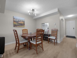 Dining area with wood-finish flooring, a contemporary ceiling light fixture, a pass-through window to the kitchen, and a paneled entry door - 