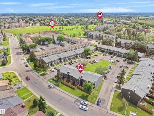 Aerial perspective showcasing a community of townhome-style residences with individual fenced yards, surface parking, and a bordering green space - 575 Dunluce Road, Edmonton, AB 