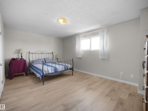 Bright bedroom featuring wood-finish flooring, light neutral wall tones, a ceiling-mounted light fixture, and a white window with sheer curtains - 575 Dunluce Road, Edmonton, AB 
