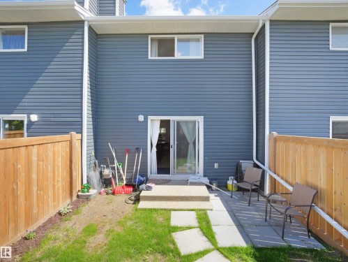 Rear exterior featuring blue horizontal siding, a private fenced yard with a concrete patio, a sliding glass door, and upper-level windows - 575 Dunluce Road, Edmonton, AB 