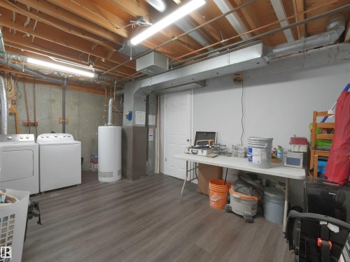 Spacious utility room featuring wood-finish flooring, exposed ceiling joists, and a white paneled door - 575 Dunluce Road, Edmonton, AB 