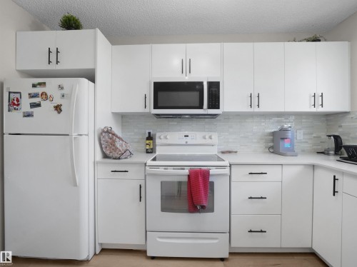 Contemporary kitchen featuring white cabinetry, black hardware, white countertops, and a white tile backsplash - 575 Dunluce Road, Edmonton, AB 