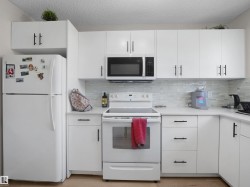 Contemporary kitchen featuring white cabinetry, black hardware, white countertops, and a white tile backsplash - 