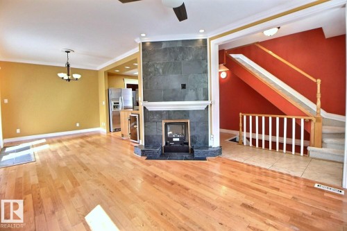 Open concept living area featuring wood-finish flooring, crown molding, and a central fireplace with slate-style tile surround - 11312 127 Street, Edmonton, AB 