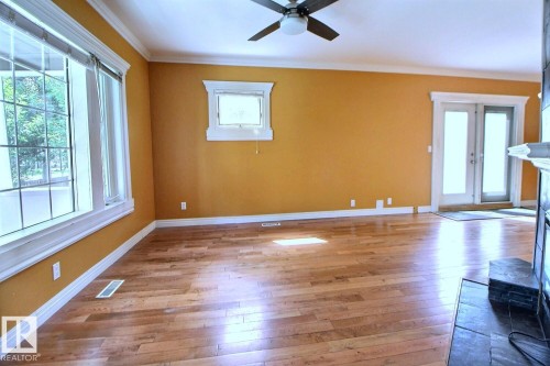 Spacious room featuring wood-finish flooring, a ceiling fan with integrated lighting, and multiple windows with white trim - 11312 127 Street, Edmonton, AB 