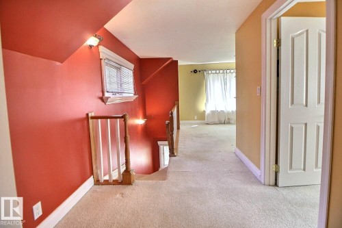 Carpeted hallway with a white panel door, white baseboards, and a window with blinds - 11312 127 Street, Edmonton, AB 