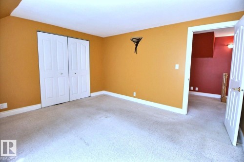 Carpeted room featuring a double bifold closet, white trim, and a wall-mounted sconce - 11312 127 Street, Edmonton, AB 