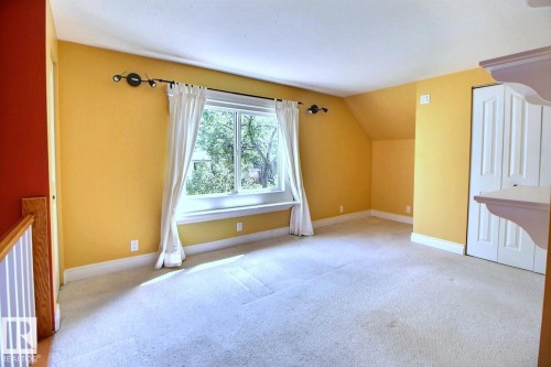 Carpeted room with a large window, white trim, bi-fold closet doors, and sloped ceiling - 11312 127 Street, Edmonton, AB 