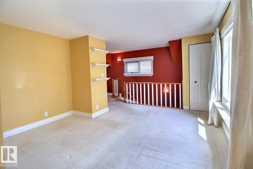 Carpeted room featuring a white banister, built-in shelving, white trim, and a white paneled door - 11312 127 Street, Edmonton, AB 