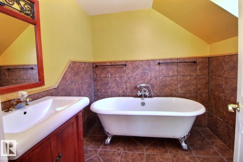Bathroom featuring a clawfoot bathtub with polished chrome fixtures, a wood-finish vanity with an integrated sink, and brown tile flooring and wainscoting - 11312 127 Street, Edmonton, AB 