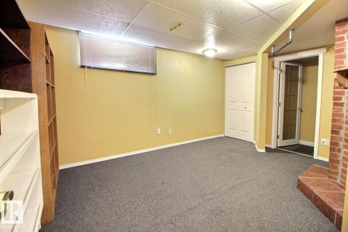 Versatile room featuring grey carpeting, built-in shelving, and a brick hearth with a tiled extension - 11312 127 Street, Edmonton, AB 