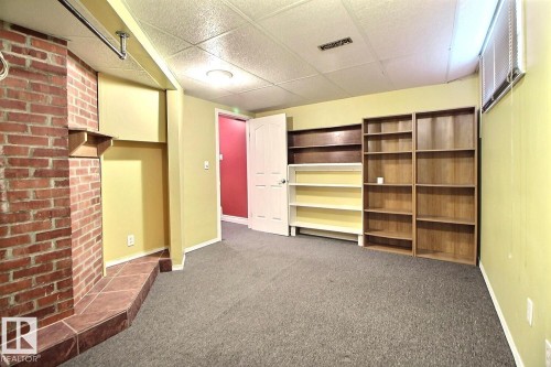 Living space featuring a brick fireplace with a tile hearth, built-in shelving, dropped ceiling, and neutral carpeting - 11312 127 Street, Edmonton, AB 