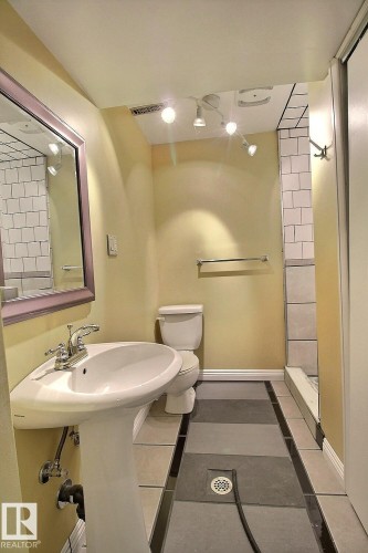 Pedestal sink with chrome faucet, track lighting, toilet, and a tiled shower stall with subway tile surround - 11312 127 Street, Edmonton, AB 