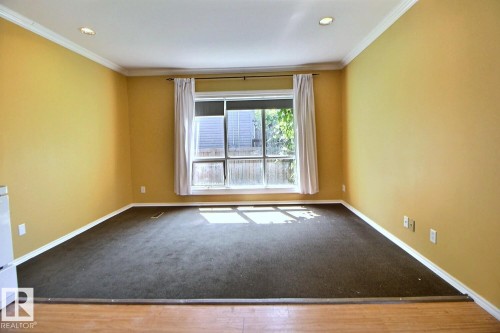 Carpeted interior space featuring a large window with white trim, recessed lighting, and a crown molding accent - 11312 127 Street, Edmonton, AB 