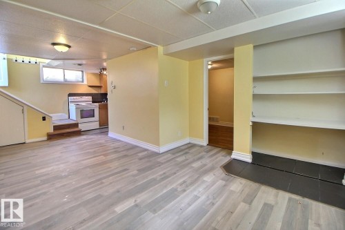 Spacious area featuring light wood-finish flooring, a full kitchen with white appliances and wood cabinetry, built-in shelving, and a tiled hearth - 11312 127 Street, Edmonton, AB 