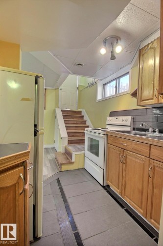 Kitchen area featuring wood-finish cabinetry, a ceramic tile backsplash, and a built-in sink - 11312 127 Street, Edmonton, AB 