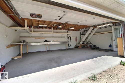 Spacious garage featuring a concrete floor, built-in workbench, overhead shelving, and a permanent staircase leading to an upper level - 11312 127 Street, Edmonton, AB 
