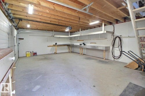 Spacious garage featuring exposed wood ceiling joists, white insulated garage door, concrete flooring, built-in shelving, and extensive workbench space - 11312 127 Street, Edmonton, AB 