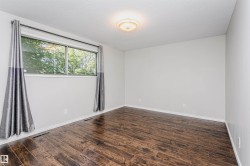 Spacious room featuring rich wood-finish flooring, a large window, neutral wall paint, white baseboards, and a ceiling-mounted light fixture - 